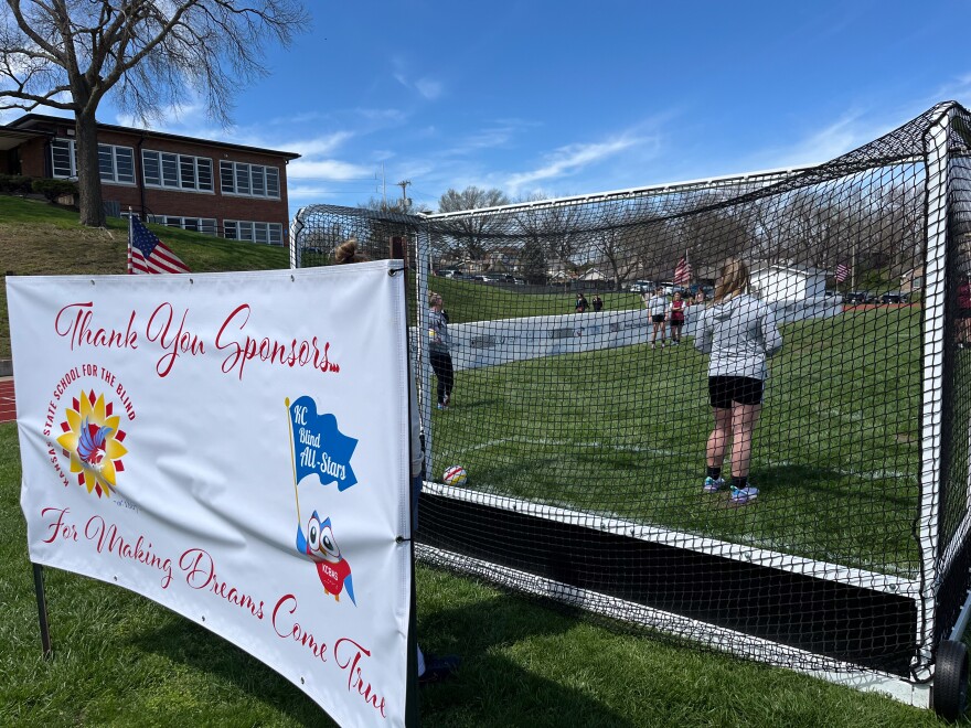 The walls of the blind soccer field are visible through the net soccer goal. A girl stands in the goal, and behind it is a banner that says "Thank you sponsors for making dreams come true" with logos from KSSB and KC Blind All-Stars.