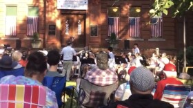 People sit in lawn chairs outside a historic brick building while a band performs on the lawn.