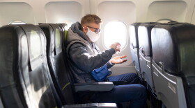 Guy in airplane with a medical protective sterile mask on his face, sitting on plane while applying sanitizer to disinfect his hands against coronavirus.