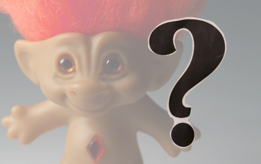 A troll doll with orange hair, a black question mark in the foreground