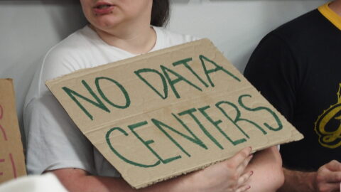 An audience member attending a Pulaski County Quorum Court agenda-setting meeting holds a sign opposing data centers on June 9, 2026.