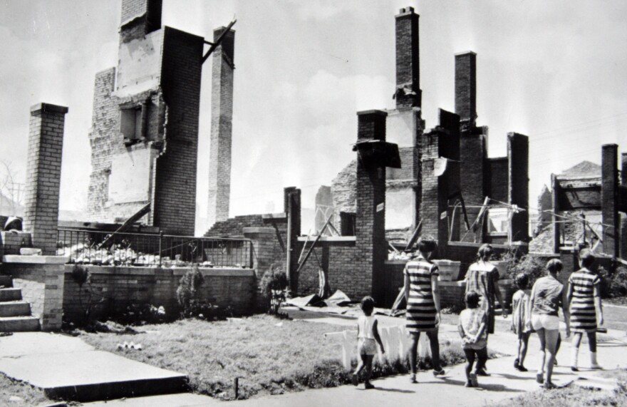 Women and children stroll past the burned remains of homes a short distance from 12th Street, which was a center of the riot activity.