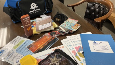 The ACPL beach-themed memory kit contains information for the caregiver, several books, photos with prompts on the back, colorful infographics, an empty sunscreen bottle, a puzzle, a plastic shovel, sunglasses and a few seashells.