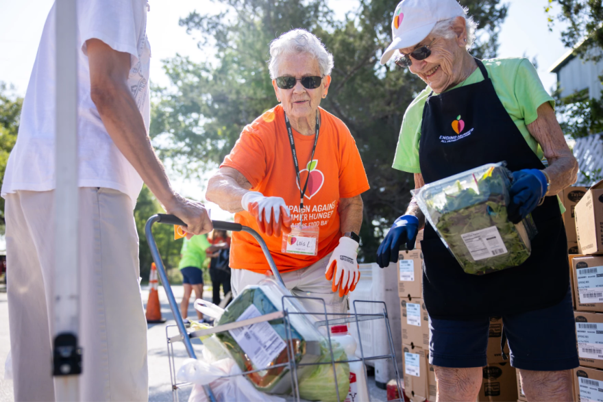 Dos mujeres cargan alimentos en un carrito de compras en un punto de distribución de alimentos móvil.