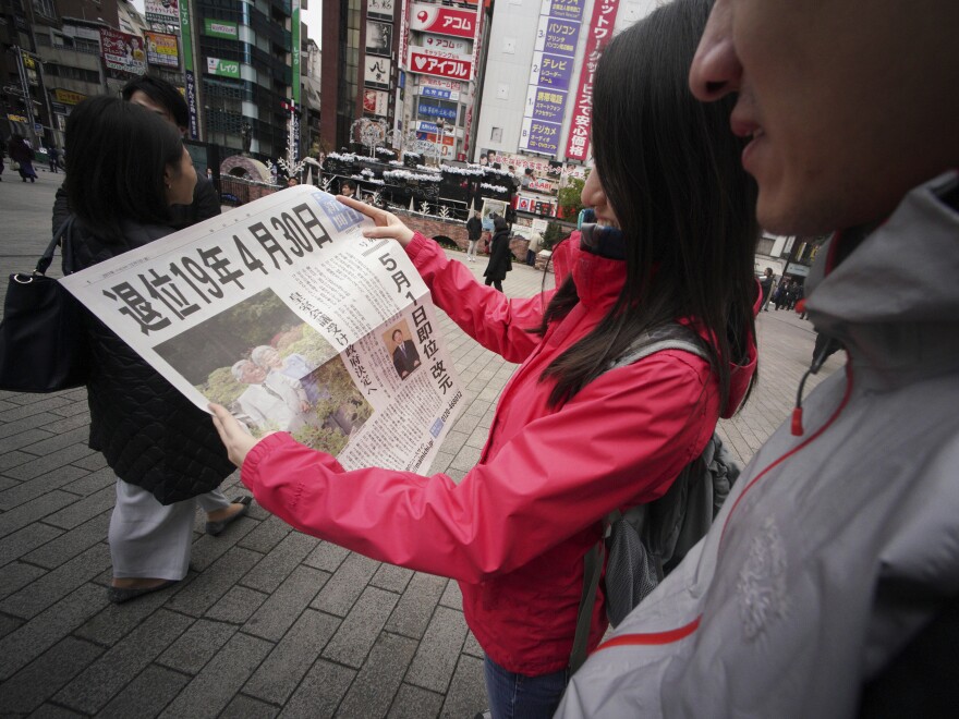 Passersby read an extra edition of a newspaper reporting Emperor Akihito's  abdicate date, at Shimbashi Station, in Tokyo on Friday.