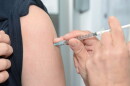 health worker sticks syringe into arm of a person with rolled up black sleeve