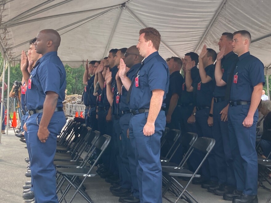 Men and women under a tent in blue uniforms hold up their right hands to take an oath.