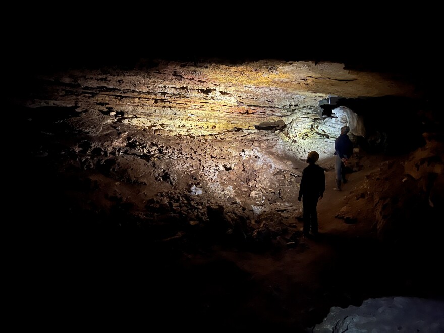 A photo shows light illuminating the inside of a cave as two people walk through it.