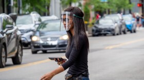A woman wears a protective face shield as she walks through downtown Cincinnati, Saturday, May 16, 2020. Local health officials say more people wearing masks will help stop the virus' spread.