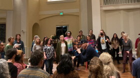 A group of about 40 people stand in a circle around a man holding a microphone.