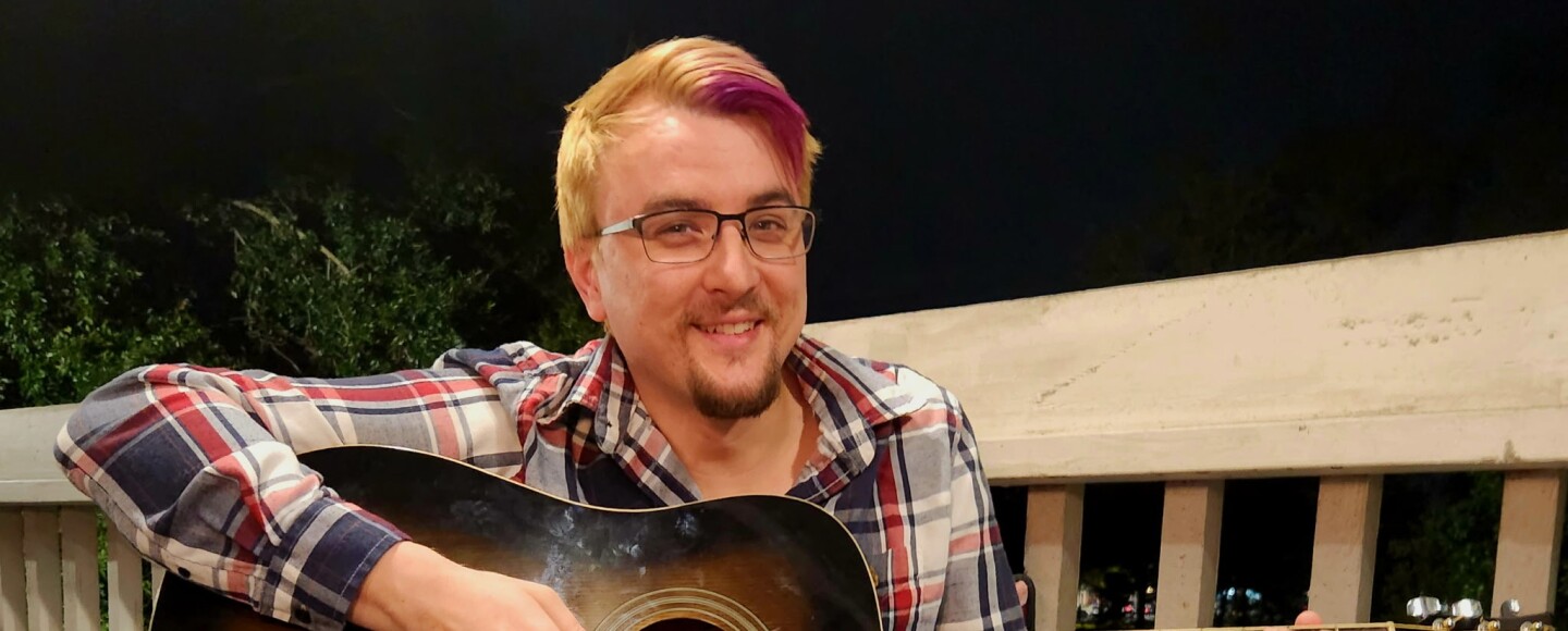 A man plays guitar and smiles for camera