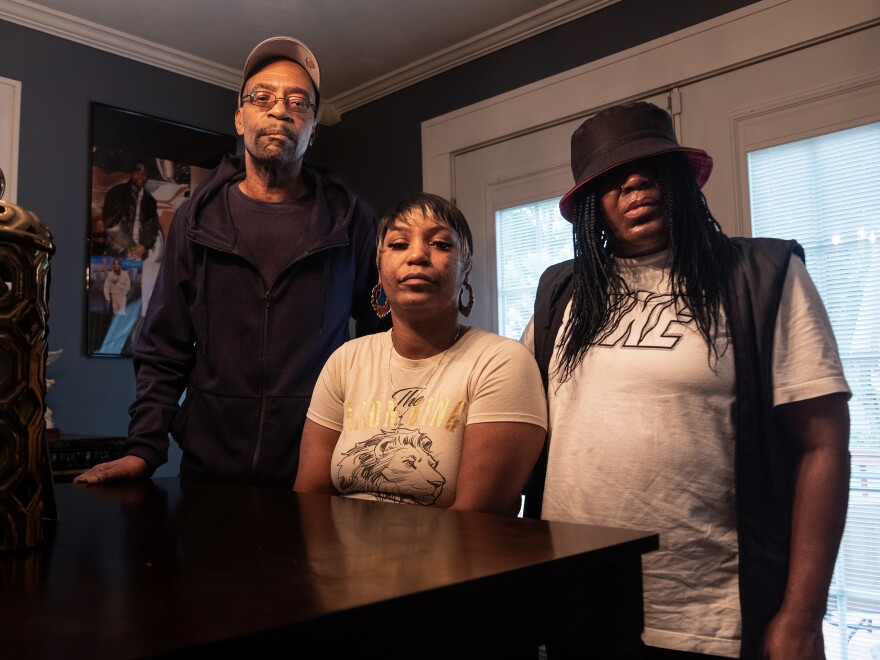 Ebony Everson (center), Bobby Everson's sister, stands with her father, who is also named Bobby Everson, and her mother Sabrina Everson. Photos of their son Bobby are on the wall behind them.