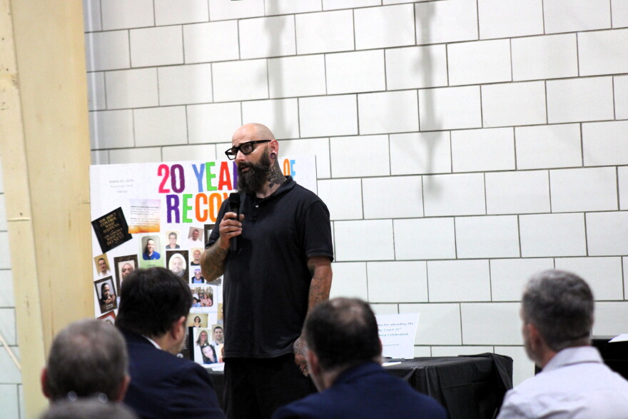 A man stands giving a speech to a crowd of seated attendees.
