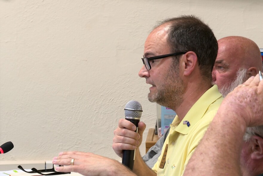 A man in a yellow shirt with glasses holding a microphone