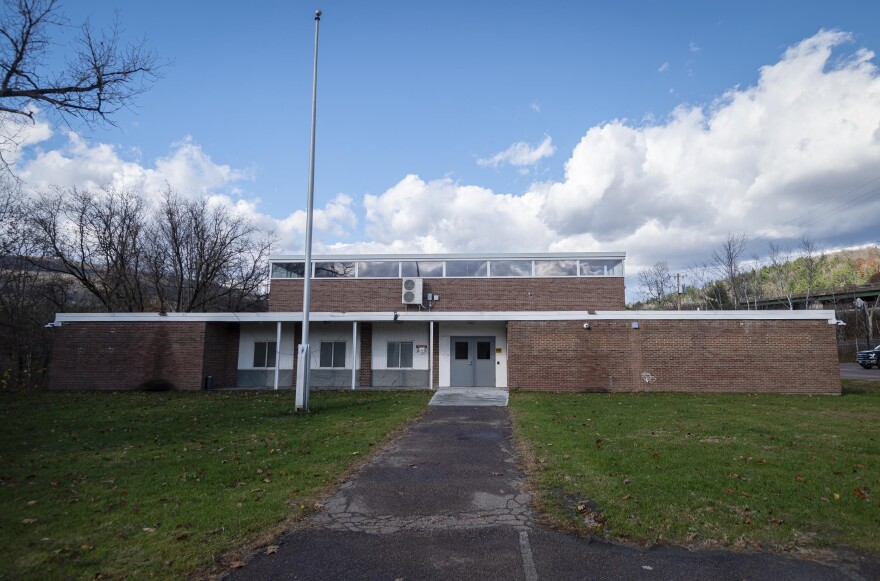 A brick building with a stark entrance stands against a blue sky with clouds in it.