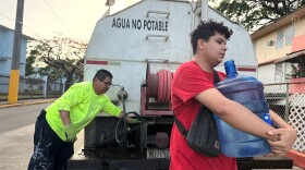 FILE - Bryan Pérez hauls a five-gallon water jug to his apartment