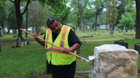 Scott Schwander uses a long-handled brush to clean the gravestone of a 9-year-old boy.