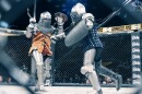 Two armored knights fight with axes and shields in a caged ring