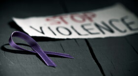 a purple ribbon for the awareness about the unacceptability of the violence against women and the text stop violence on a piece of paper, on a dark gray rustic wooden surface