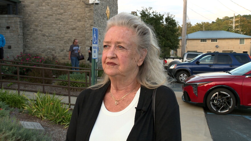 A woman stands in front of a brick building.