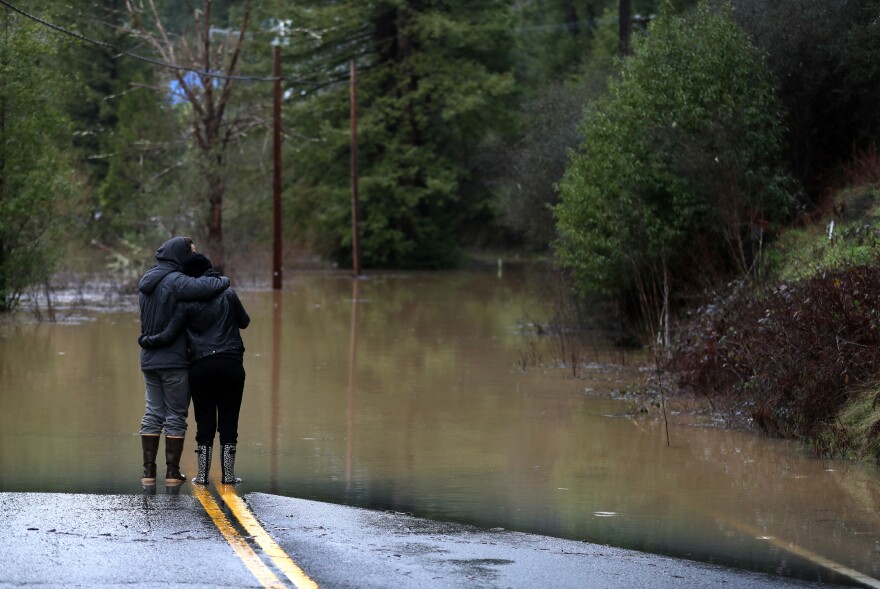 Ari Herman (left) and Lea Herman embrace as they look at a flooded section of State Route 116 in Guerneville.