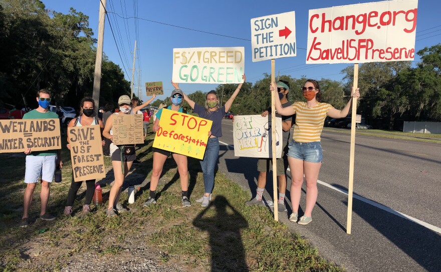 About seven people wearing masks holding various protest signs on the shoulder of a road. 