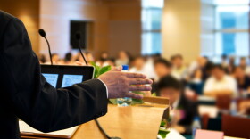Business man is making a speech in front of a big audience at a conference hall. 