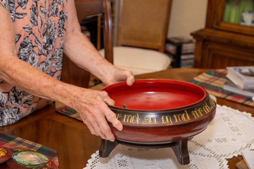 A bowl with a red interior and legs that has an inscription around the top in gold letters.