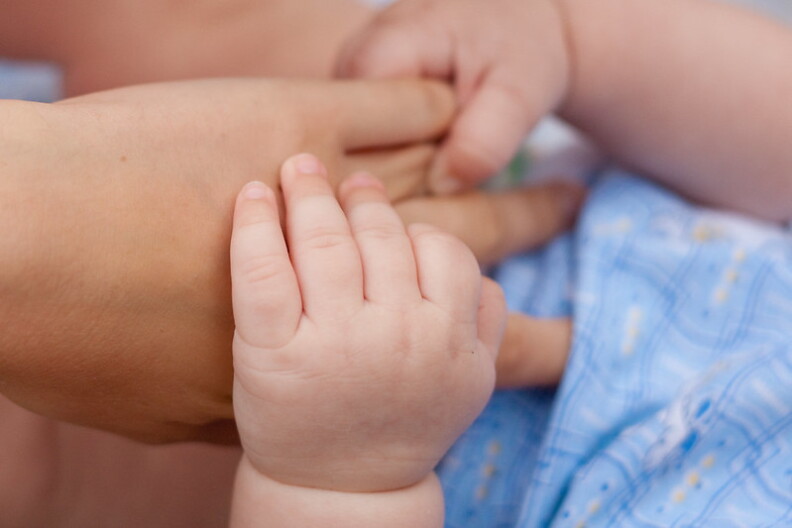 Two small hands hold on to a larger hand.