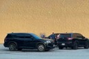  Three black unmarked SUVs parked next to a blank exterior wall with several people standing outside one of them closest to the wall. 