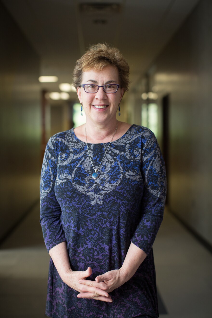 Portrait of author Michelle Miller Adams. She is standing in a hallway, wearing a blue patterned dress and smiling