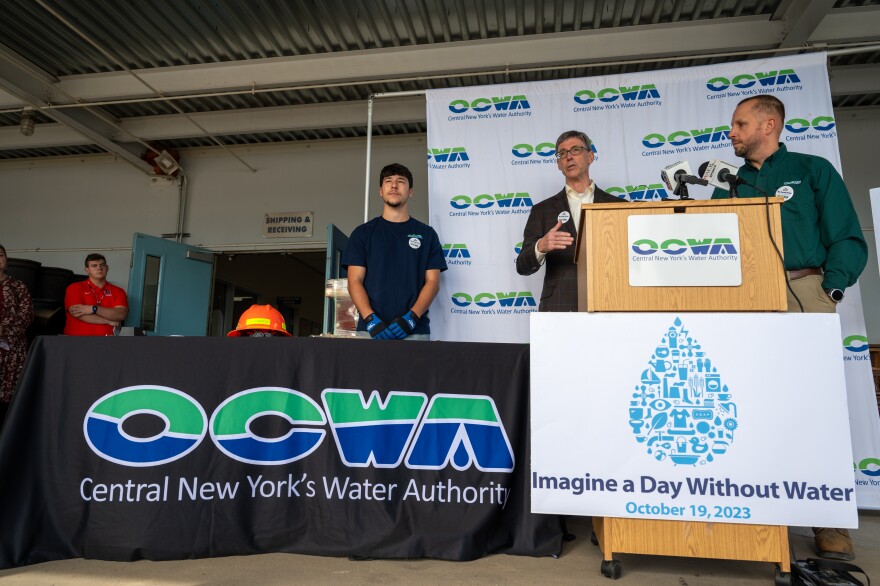 Four people stand behind a table and a lectern with the letters OCWA.