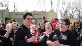 People wearing black t-shirts and hoodies smile while one person holds a red envelope