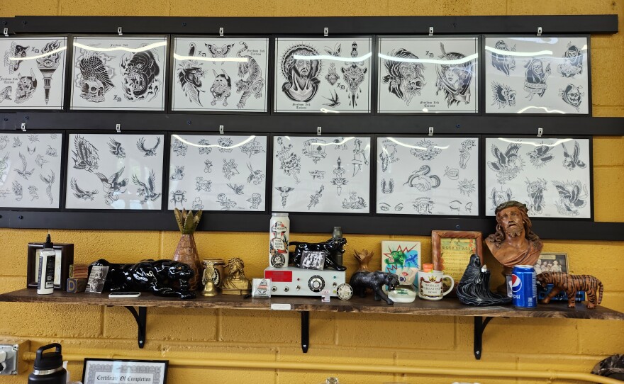 Images of tattoos hang on a wall above a shelf of eclectic items.