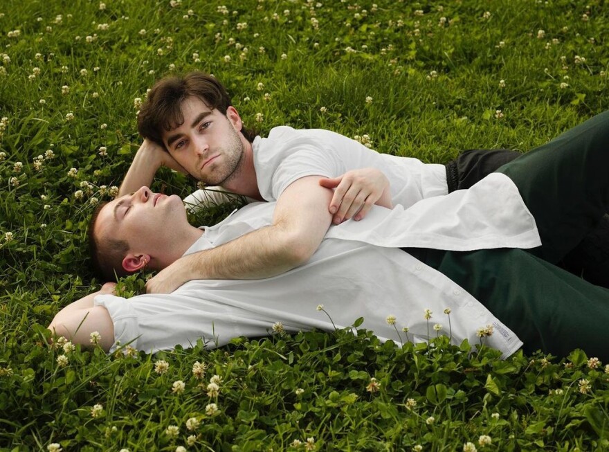 A couple embraces while laying down in a field of grass and flowers.