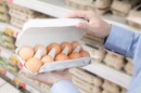 This stock image shows a man checking a carton of eggs in the supermarket.