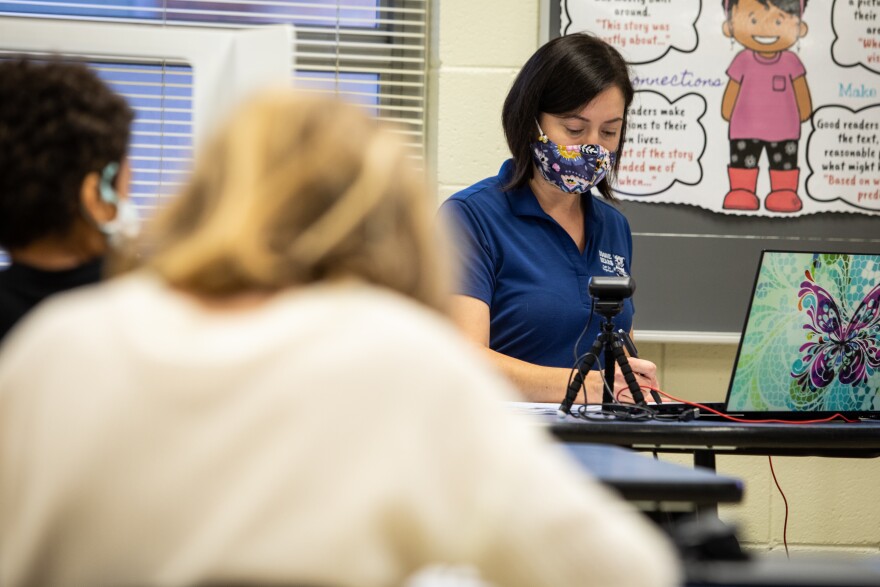 A teacher teaches a hybrid class to in-person and remote students from her classroom. 