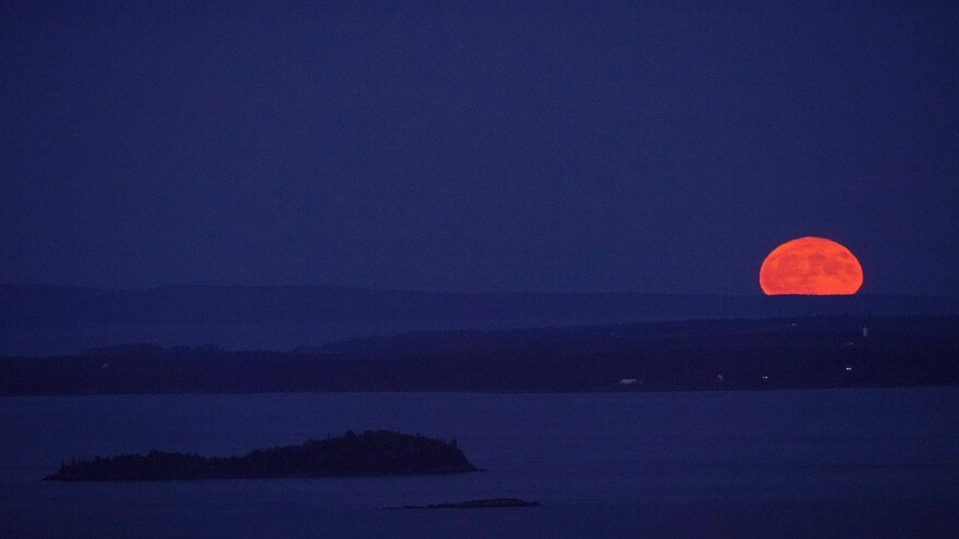 The supermoon ascends into the sky with Isle Au Haut in the distance and North Haven Island in the middle ground, as viewed from Camden, Maine.