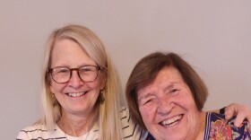 Nancy Antle has long white hair. She wears glasses and jeans with a white tee shirt with narrow, horizontal, black stripes. She has a silver pendant around her neck.  Nancy smiles and has one arm around her stepmother, Georgia Thompson  Nancy is half a head taller than Georgia.  Georgia smiles broadly and has short brown hair. She wears a navy blue top with a large orange and green floral pattern.