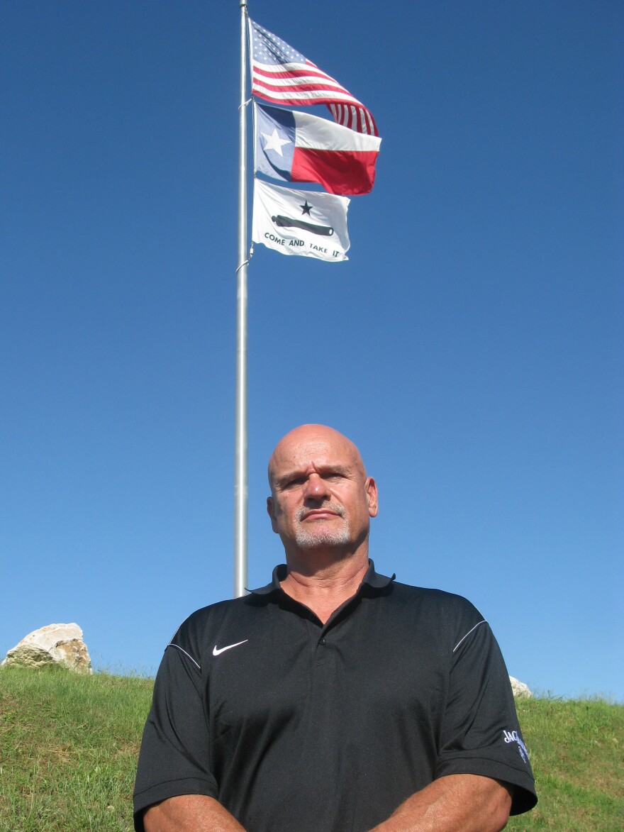 Max Bordelon stands beneath the U.S. flag, Texas flag and "Come and Take It" flag. He says he flies the "Come and Take It" flag in front of his restaurant as a protest against government overreach.