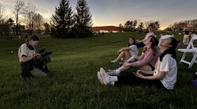 Producer Claire Hannah Collins films students sitting on a grassy hill during sunset on the set of the Greenacres documentary project.