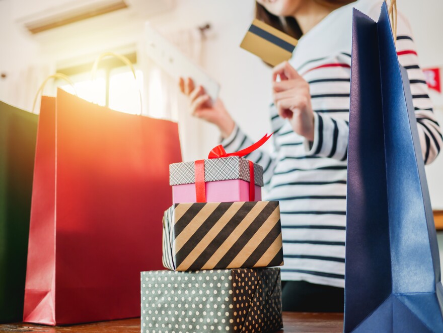 Picture of a woman holding tablet and credit card, shopping bags with gift box on wooden table, Christmas shopping.