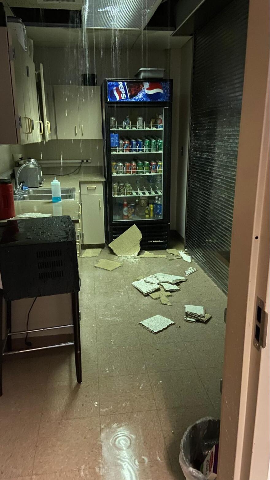 Water leaks from a ceiling and floods a room with ceiling tiles on the floor. 