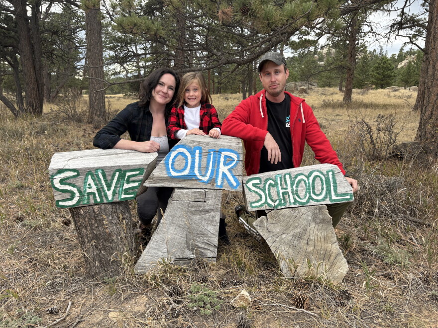 Three people lean against three pieces of wood, with the words "Save Our School."