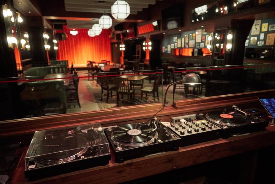 A view of the turntables and sound system with tables, chairs and a stage in the background.