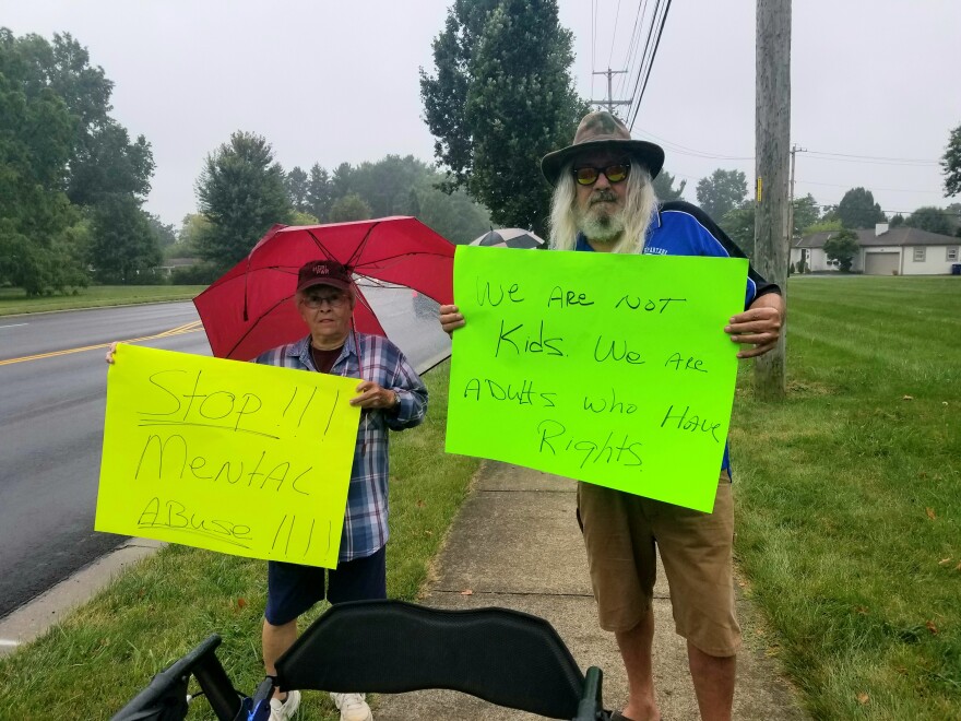 Two people hold cardboard signs reading "Stop mental abuse" and "We are not kids. We are adults who have rights." 