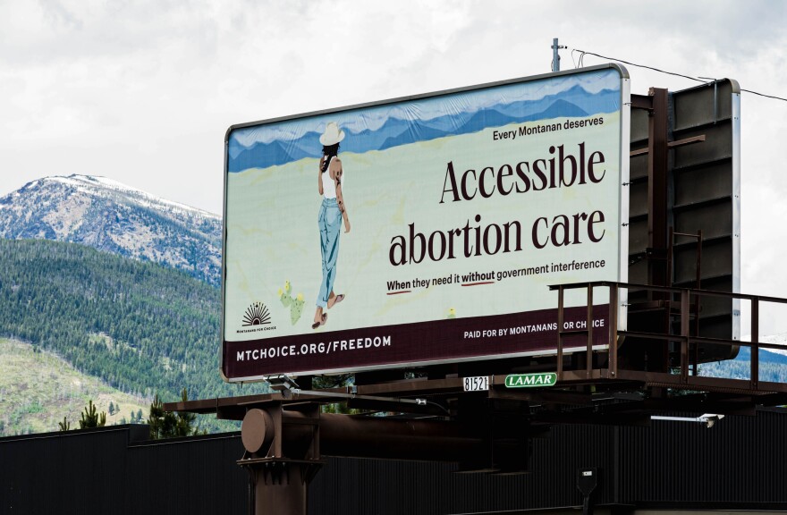 A sign featuring an illustration of a woman standing in front of a mountain range with the words "All Montanans deserve access to affordable abortion whenever they need it, without government interference."