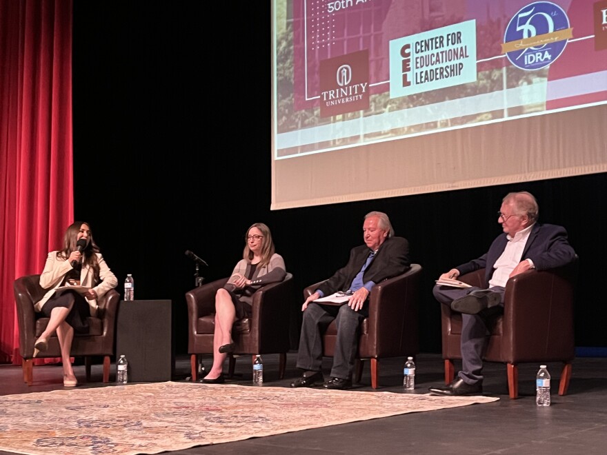 Two women and two men sit in chairs on a stage talking on a panel.