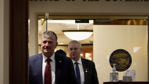 Two men in suits walk down a hallway.