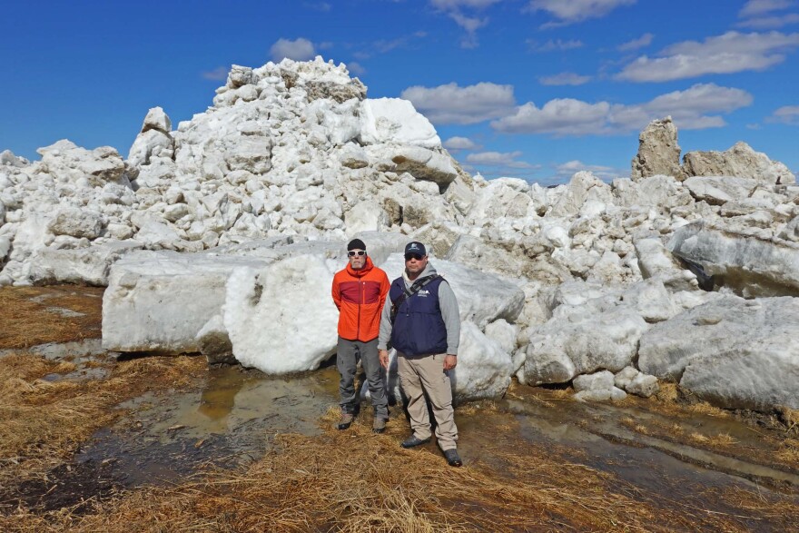 National Weather Service hydrologist Johnse Ostman, left, and Willis Walunga with the Alaska Department of Homeland Security and Emergency Management pose in front of an ice pushed up over the bank by the Kuskokwim River on May 8, 2026.